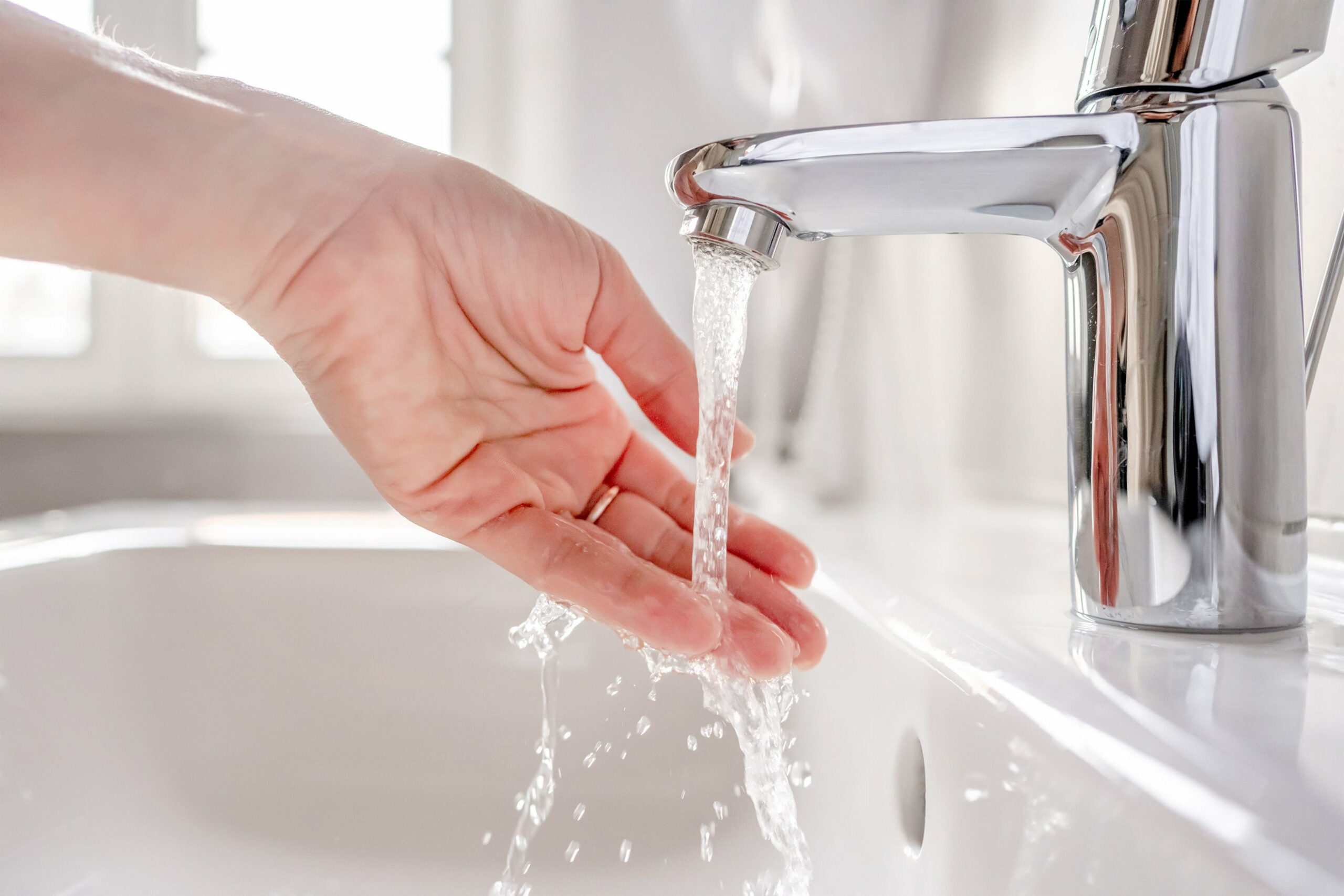 Young woman washes her hands with soap over the sink in the bathroom, close-up.